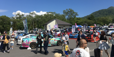 image of a Japanese car she where cars are parked and people are watching cars