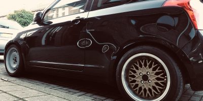 image of suzuki swift with steel wheels up front and golden spoke wheels at the back