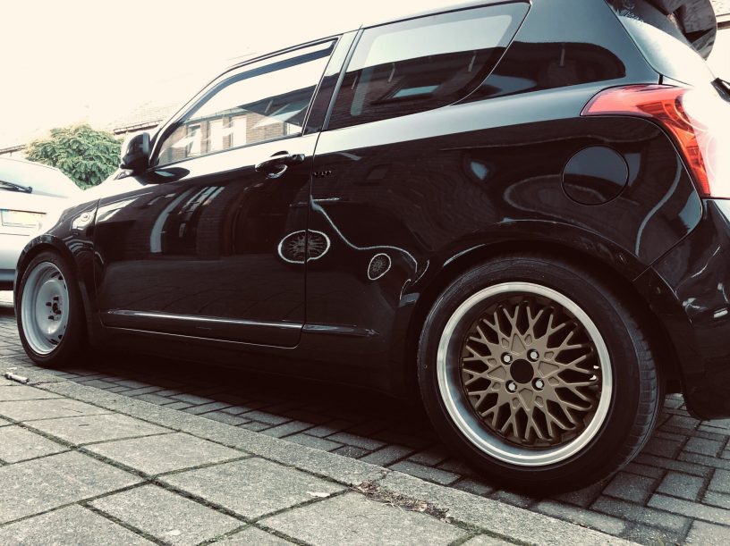 image of suzuki swift with steel wheels up front and golden spoke wheels at the back