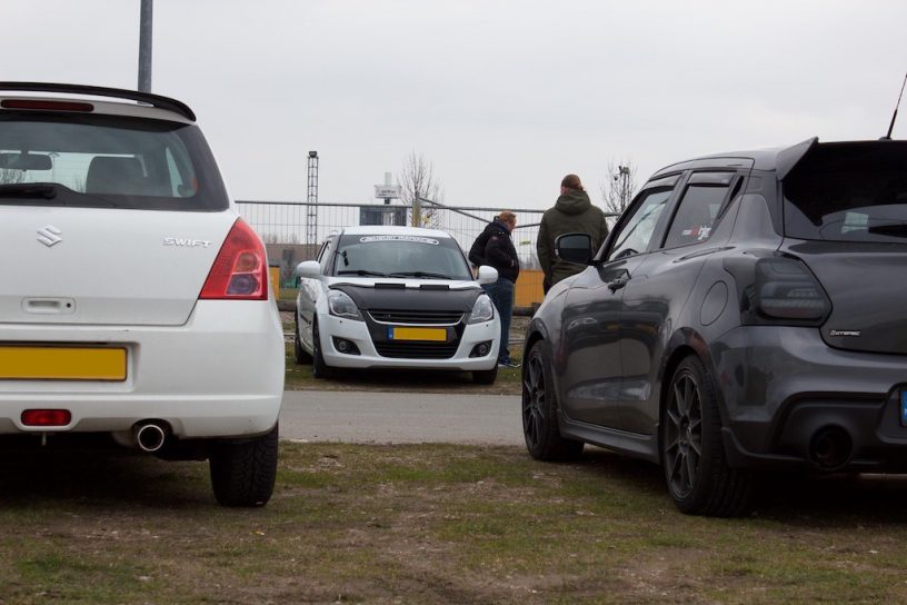 3 suzuki swift cars parked on a grass field and people walking around