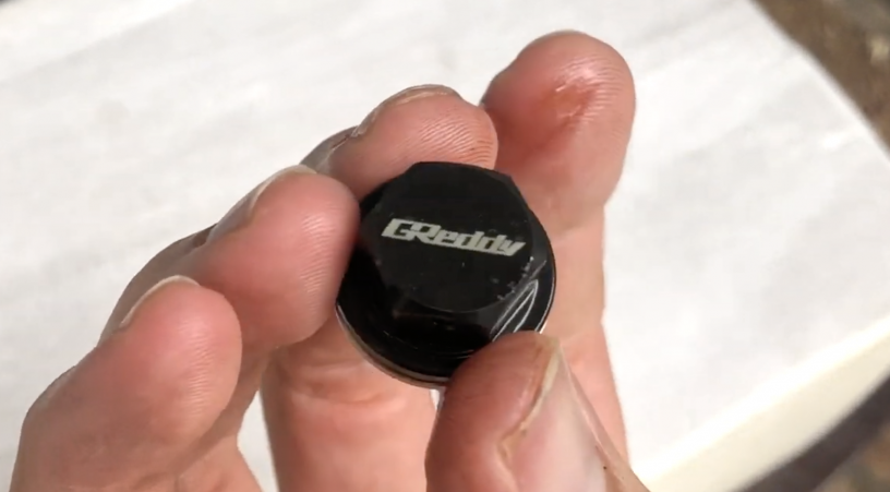 Hand holding a used greddy oil drain plug